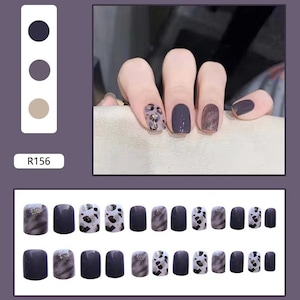 May include: A set of press-on nails in various designs. The nails feature a dark purple hue, leopard print, and a marbled effect. The image also shows a hand with the nails applied, and a color palette.