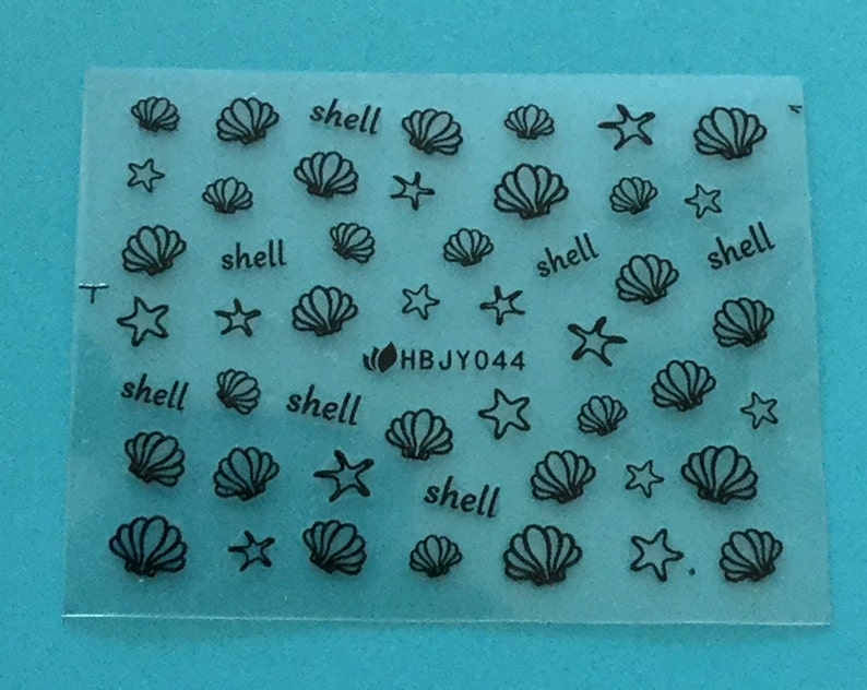 May include: A sheet of clear nail decals with black outlines of seashells and starfish. The sheet has the text "shell" repeated multiple times and the code "HBJY044".