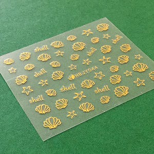 May include: A sheet of clear nail decals with gold seashells and stars. The sheet has the text "HBJY044" and "shell" repeated multiple times.