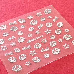 May include: A sheet of clear nail art stickers with white seashells and starfish designs. The sheet includes the text "shell" and "HBJY044".