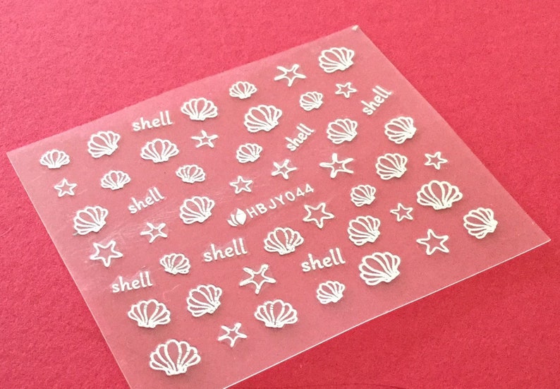 May include: A sheet of clear nail art stickers with white seashells and starfish designs. The sheet includes the text "shell" and "HBJY044".