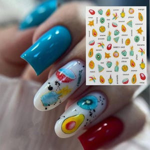 Könnte beinhalten: Nagelkunst-Aufkleber mit farbenfrohen Fruchtdesigns, darunter Mangos, Kiwis und Avocados. Die Aufkleber enthalten auch den Text "summer" und "HANY1-662". Die Nägel sind mit glänzendem blauem, weißem und rotem Nagellack lackiert.