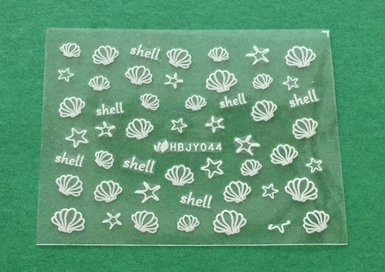May include: A sheet of white nail decals with images of seashells and starfish. The sheet has the text "shell" printed five times and the code "HBJY044" printed once.