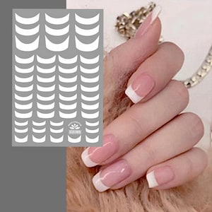 May include: A sheet of white nail art stickers with a French tip design. The stickers are arranged in rows and columns. The image also shows a hand with French tip nails.