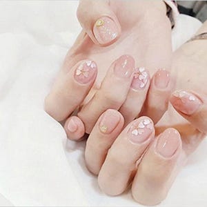 Puede incluir: Primer plano de manos con esmalte de uñas de color nude y delicado arte de uñas con flores blancas.