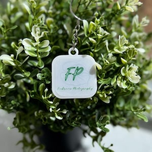 May include: White square keychain with a green logo that says "FP" and "Fissure Photography".