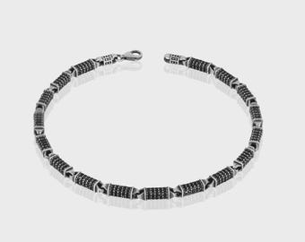 May include: A silver-toned necklace with a series of cylindrical links, each encrusted with small, black stones. The necklace has a lobster clasp closure. The design is symmetrical and the necklace is displayed on a white background.