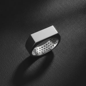 May include: A silver-toned ring featuring a flat, rectangular top surface and a smooth, polished exterior. The interior of the band is detailed with a repeating hexagonal honeycomb pattern, providing a textured contrast to the sleek outer metal finish.