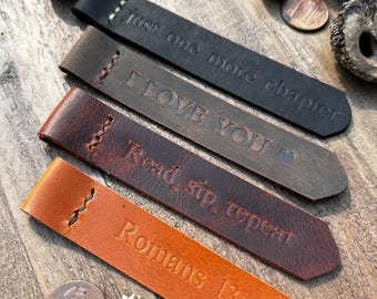 May include: Four leather bookmarks with different sayings. The bookmarks are brown, black, and orange. The sayings are "Just one more chapter", "I love you", "Read, sip, repeat", and "Romans 13:10".