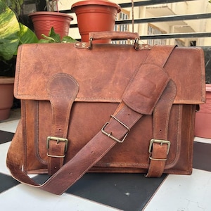 May include: A brown leather briefcase with a long adjustable shoulder strap and two buckles on the front. The briefcase has a top handle and a flap closure.