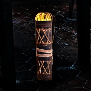 May include: A brown leather quiver with a strap and decorative stitching. The quiver is empty and has a worn look.