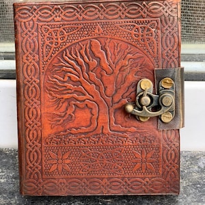 May include: A brown leather journal with a tree of life design and a Celtic knot border. The journal has a brass clasp and is closed.