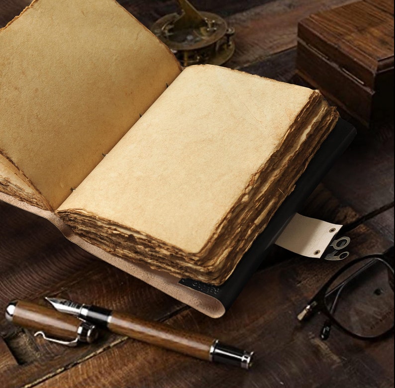 May include: A vintage leather-bound journal with blank pages, open to reveal the aged paper. The journal is lying on a wooden surface with a pair of glasses and a pen nearby.