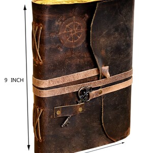 May include: A brown leather journal with a compass design on the front cover. The journal has a key and a leather strap closure. It measures 9 inches tall and 6 inches wide.