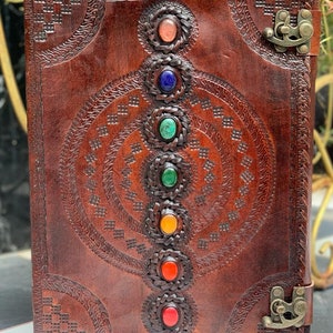 May include: Brown leather journal with a decorative design and seven colorful gemstones. The journal has two clasps on the front and back covers.