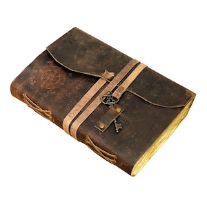 May include: A brown leather journal with a compass design and a key charm. The journal has two straps and is tied closed with laces.