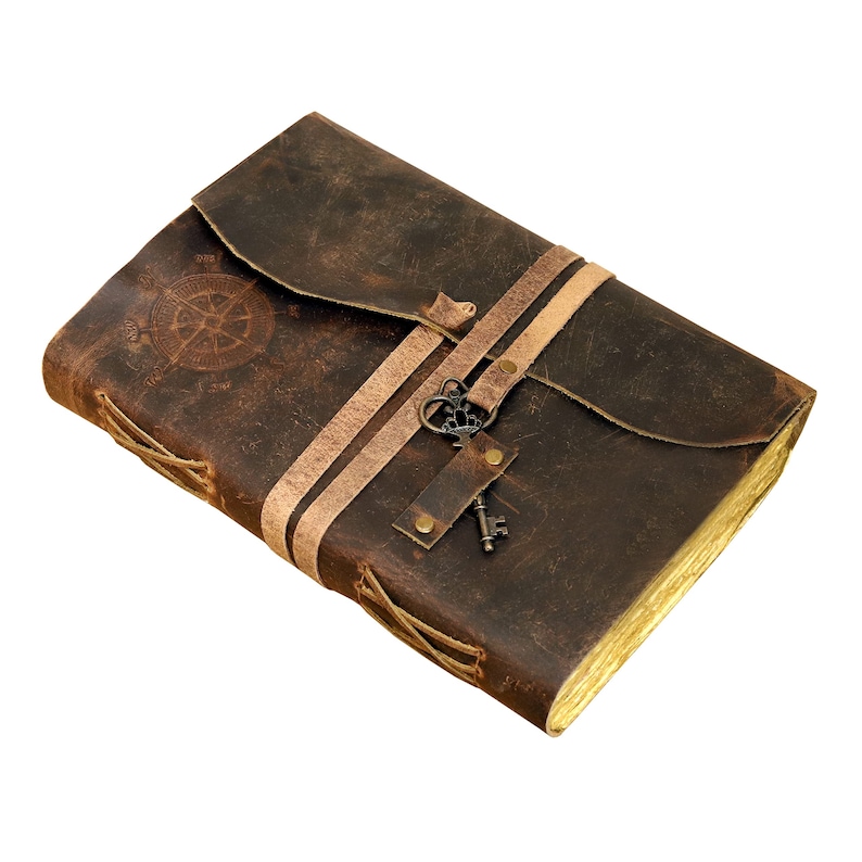 May include: A brown leather journal with a compass design and a key charm. The journal has two straps and is tied closed with laces.