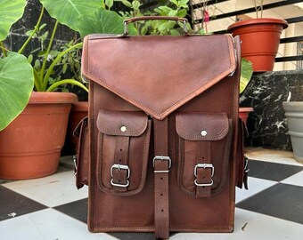 May include: A brown leather backpack with two large front pockets and buckles. The backpack has a top handle and adjustable straps.