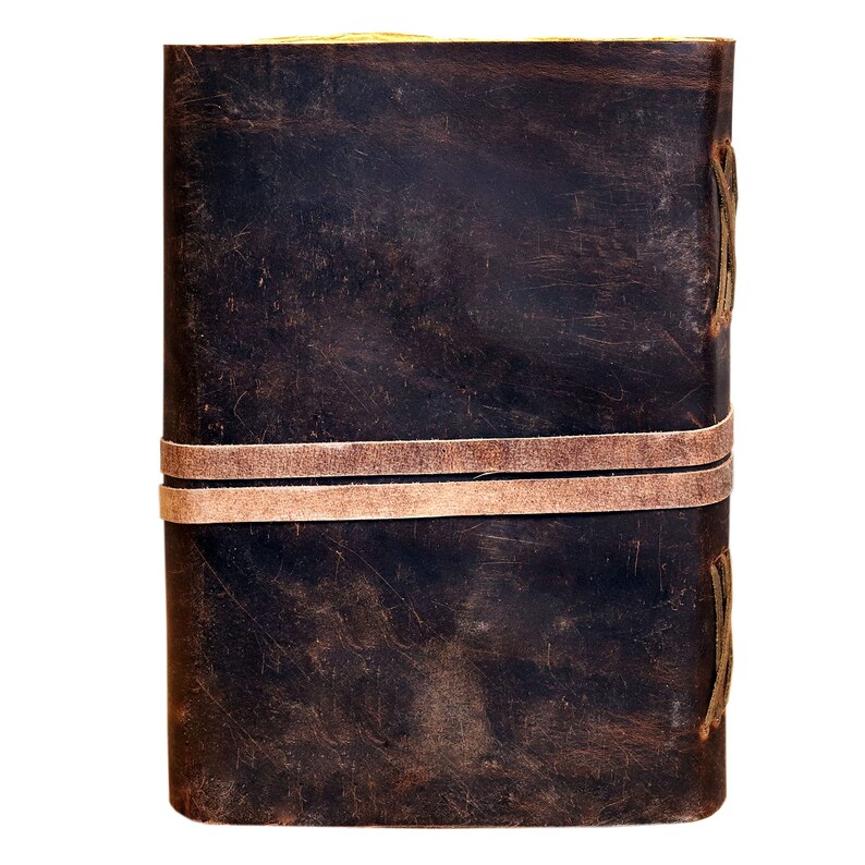 May include: A dark brown leather-bound journal with two brown leather straps and stitching detail. The journal has a worn, vintage look.