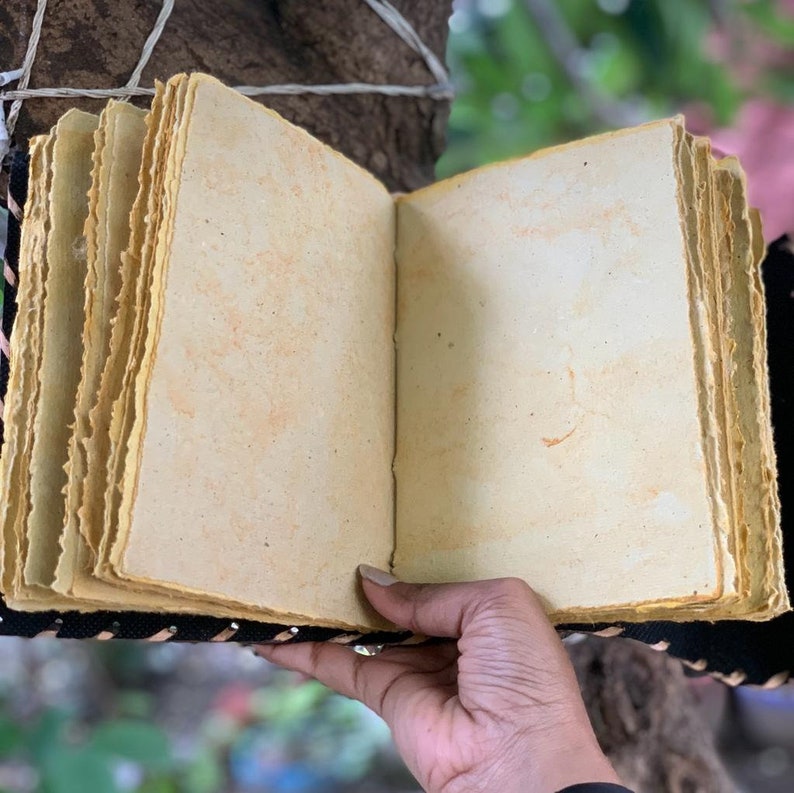 Puede incluir: Un diario hecho a mano abierto, con p&aacute;ginas envejecidas de color crema. Las p&aacute;ginas tienen un borde rugoso y recortado y se guardan dentro de una cubierta negra con costuras decorativas. El diario est&aacute; abierto, mostrando las p&aacute;ginas en blanco.