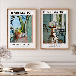 Peut inclure: Deux tirages d'art encadrés représentant des peintures d'Henri Matisse. L'impression de gauche est "La Terrasse, St. Tropez" et celle de droite est "La Fenêtre". Les deux tirages sont dans des cadres en bois et sont accrochés au-dessus d'un bureau en bois.