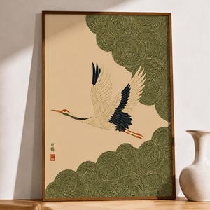 Peut inclure: Une impression d'art encadrée représentant une grue blanche en vol sur un fond beige clair. La grue a le bout des ailes noir et une couronne rouge. Des motifs de nuages circulaires verts stylisés sont placés dans les coins.