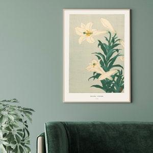 May include: A vintage Japanese woodblock print of white lilies with green leaves on a light blue background. The print is titled "Ohara Koson" and is framed in a white frame.