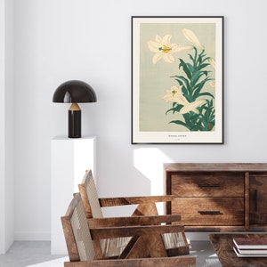 May include: A vintage Japanese woodblock print of white lilies with green leaves on a light blue background. The print is framed in black and has the text "OHARA SOSON" and "1928" in the bottom right corner.