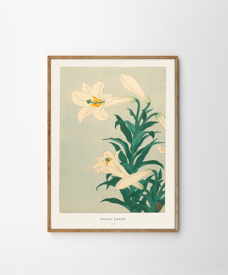 May include: A vintage Japanese woodblock print of white lilies with green leaves against a light blue background. The print is framed in a light brown wood frame. The artist's name, "Ohara Koson", is printed in the bottom right corner of the print.