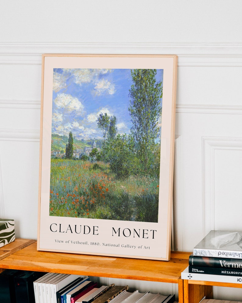 Op de afbeelding: Een ingelijste kunstprint van een schilderij van Claude Monet met de titel "Uitzicht op Vetheuil, 1880." Het schilderij toont een landschap met een veld rode klaprozen op de voorgrond, een dorp in de verte en een blauwe lucht met witte wolken.