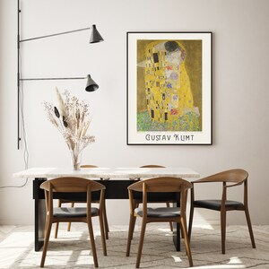 Pu&ograve; includere: Un poster del dipinto "Il Bacio" di Gustav Klimt, che rappresenta due figure che si abbracciano in un motivo dorato a mosaico. Il poster &egrave; incorniciato e appeso a una parete bianca sopra un tavolo da pranzo con quattro sedie.