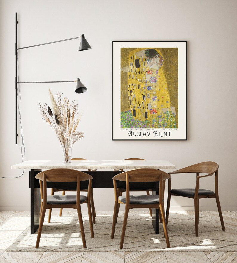 Pu&ograve; includere: Un poster del dipinto "Il Bacio" di Gustav Klimt, che rappresenta due figure che si abbracciano in un motivo dorato a mosaico. Il poster &egrave; incorniciato e appeso a una parete bianca sopra un tavolo da pranzo con quattro sedie.