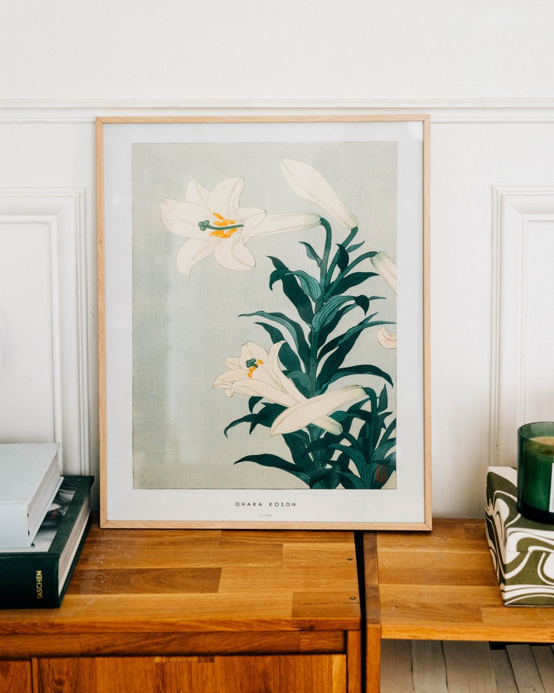 May include: A framed print of a Japanese botanical illustration featuring white lilies with green leaves. The print is titled "Ohara Koson" and is in a light wood frame.