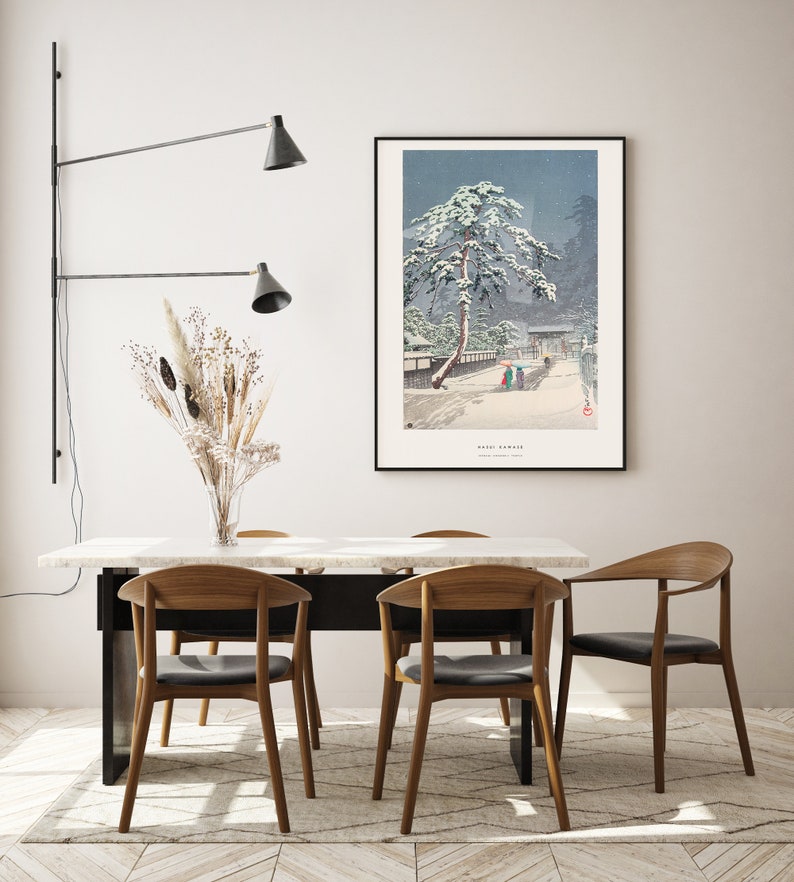 May include: A dining room with a white marble table and four wooden chairs. A black wall-mounted light fixture with two shades is on the left side of the image. A framed print of a snowy Japanese landscape hangs on the wall behind the table. The print features a pine tree covered in snow and the text "Yuki-Yama" in the bottom right corner.