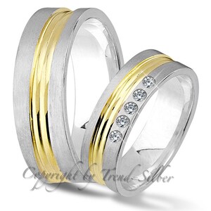 Könnte beinhalten: Zwei Eheringe, einer mit gebürsteter Silberoberfläche und einem goldenen Band, der andere mit gebürsteter Silberoberfläche und einer Reihe kleiner Diamanten.