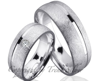 May include: A pair of silver wedding bands with a brushed finish and a single diamond on one band. The bands have a thin, polished line down the center.