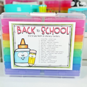 May include: A clear plastic storage container filled with colorful, labeled trays for 3rd-grade math and literacy centers. The container features a label with the text "BACK to SCHOOL" and a cartoon glue bottle and pencil.