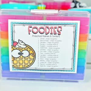 May include: A colorful storage box with a list of food-themed preschool games and centers. The list includes activities like shape recognition, counting within 10, and counting within 20. The box is labeled "Foodies Preschool Games & Centers".