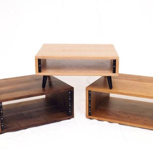 May include: Three wooden audio rack cabinets in different wood tones. The top cabinet is light-colored, the left is dark brown, and the right is medium brown. Each has black legs and black metal strips on the sides.