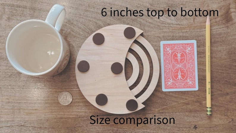 May include: A wooden coaster with a crescent design, featuring brown circular pads. The image includes a playing card, a pencil, a coffee mug, and a coin for size comparison. The coaster is 6 inches from top to bottom. The text "Size comparison" is also visible.