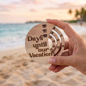 May include: A circular wooden countdown calendar with the text "Days until our Vacation" engraved on the front. The device features three rotating concentric rings with numbers 0 through 9, allowing for manual adjustment of the displayed day count.