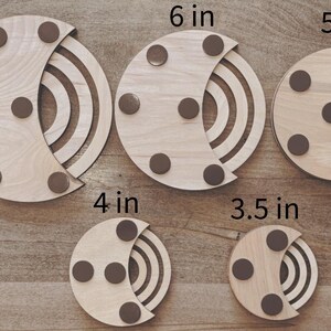 May include: A collection of five wooden coasters in varying sizes, ranging from 3.5 inches to 7 inches in diameter. Each coaster features a light wood finish, a crescent-shaped design, and brown circular pads.