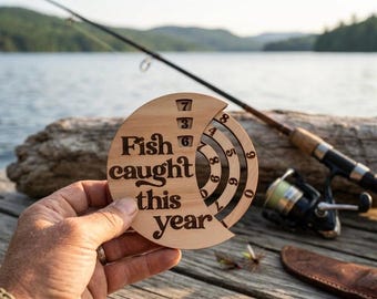 May include: A circular light-colored wooden tracker with the engraved text "Fish caught this year". The design features three concentric rotating rings with numbers zero through nine, allowing for manual adjustment to display a specific count.