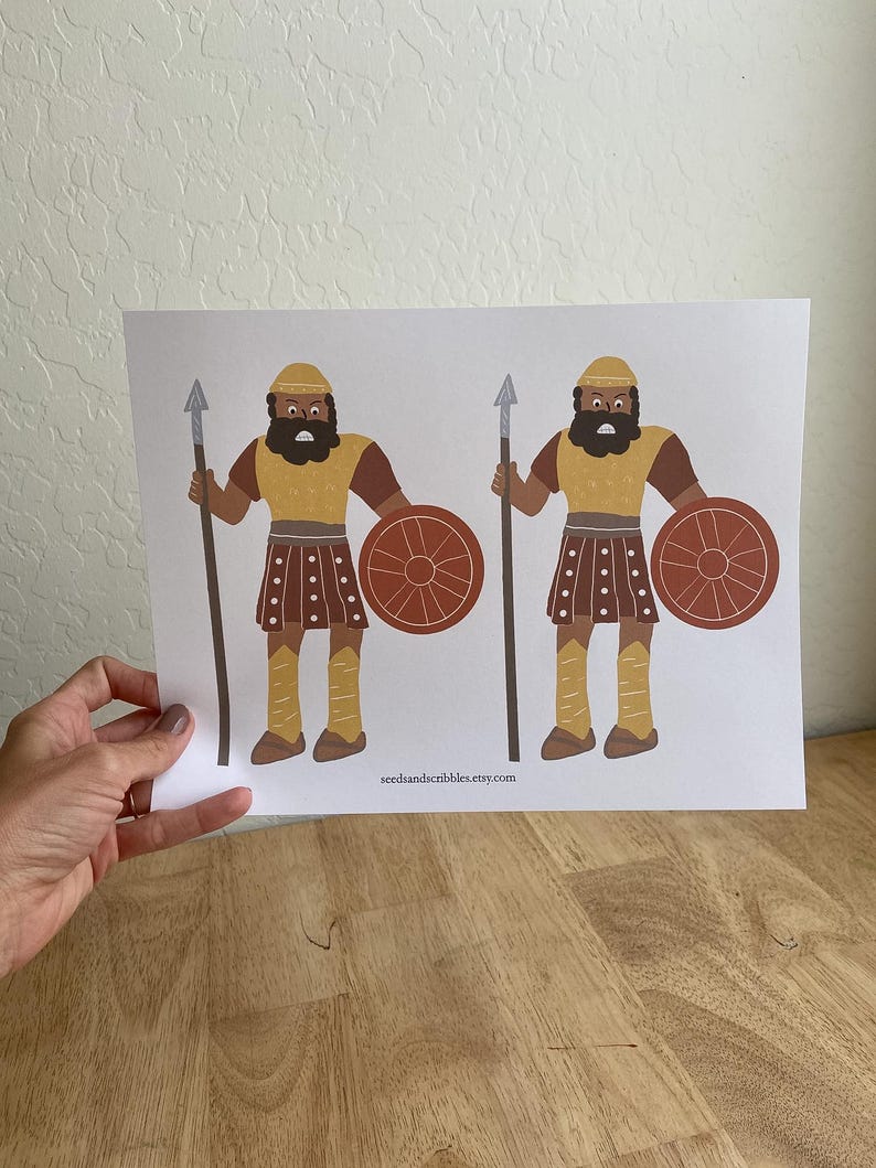 May include: A print featuring two cartoon illustrations of warriors. Each figure is depicted with a spear, shield, and wearing a yellow helmet and tunic, brown sleeves, and brown skirt. The shield is a reddish-brown color. The website address "seedsandscribbles.etsy.com" is printed at the bottom.