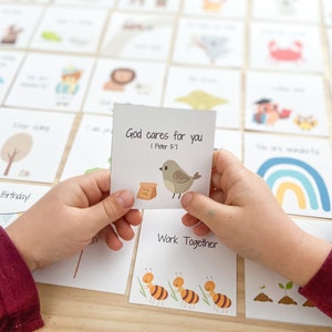 May include: A child's hand holds a card with a small bird illustration and the text "God cares for you 1 Peter 5:7". The card is one of many cards with different illustrations and messages.