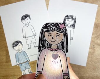 May include: A paper cutout of a person with long dark hair wearing a pink dress with a heart graphic on the chest, illuminated from behind. In the background, two white sheets of paper feature black and white line drawings of people.