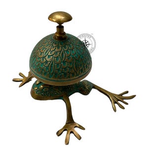May include: A brass frog-shaped service bell with a green patina finish. The bell has a domed top with an intricate design and a brass knob.