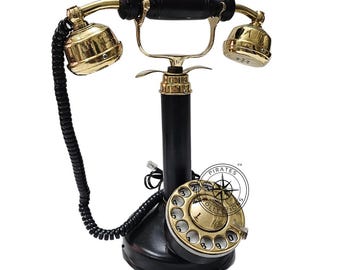 May include: A black rotary dial phone with a gold-colored base and receiver. The phone has a black cord and a gold-colored dial with numbers 1 through 0. The phone is on a white background.