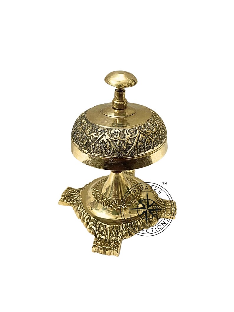 May include: A gold-toned brass service bell with an ornate design. The bell has a round top with a knob on top and a base with four decorative feet.