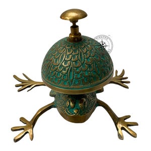 May include: A brass frog-shaped door bell with a green and gold dome. The dome has a decorative pattern and the frog has outstretched legs.